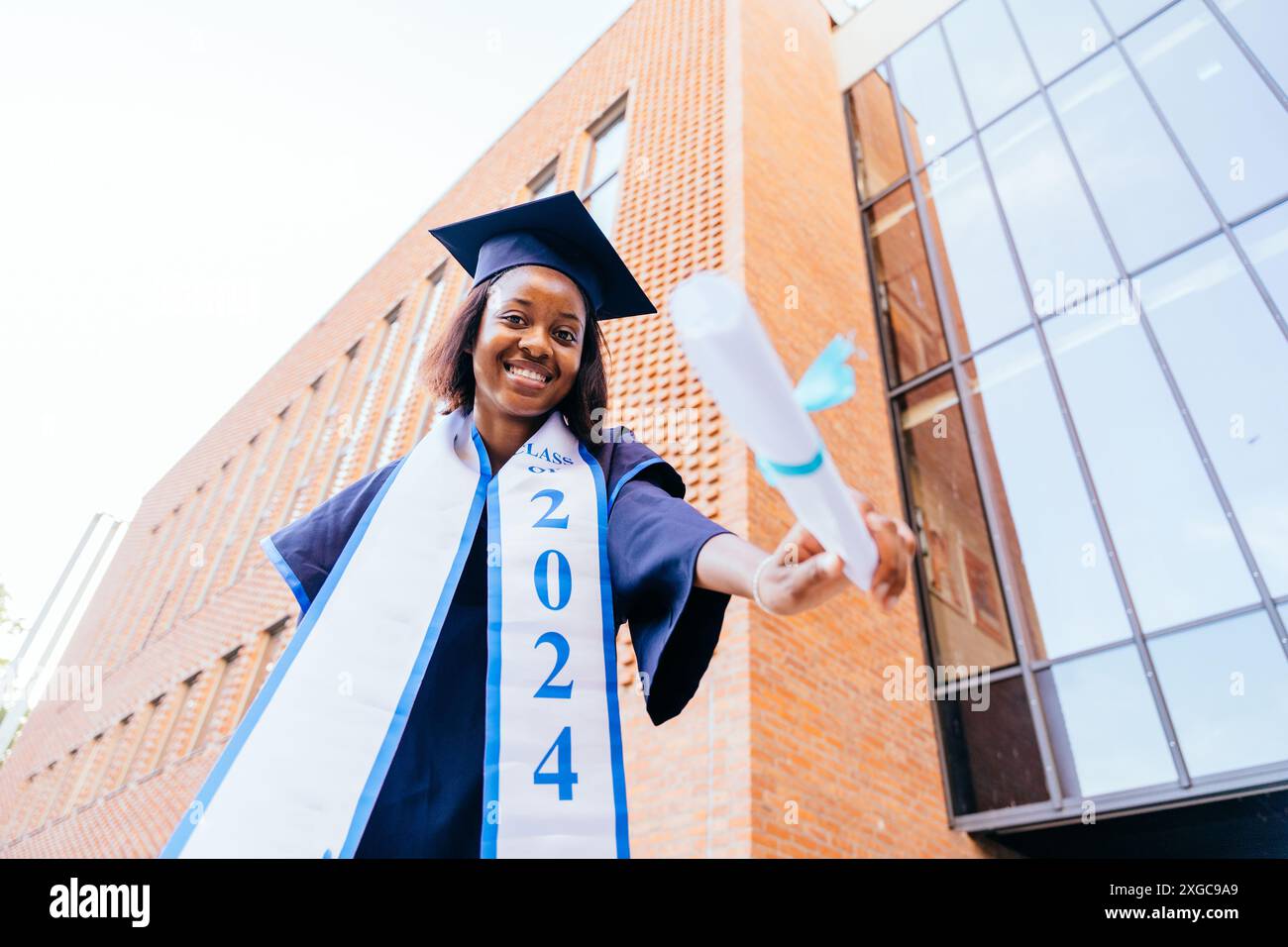 African student woman in a graduation gown showing to camera diploma ...