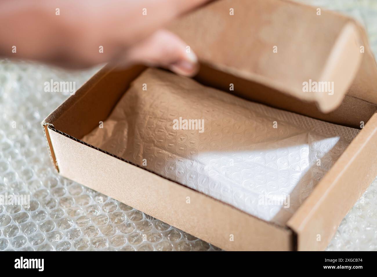 A person opening a cardboard box with bubble wrap inside, placed on a bubble wrap sheet. Stock Photo