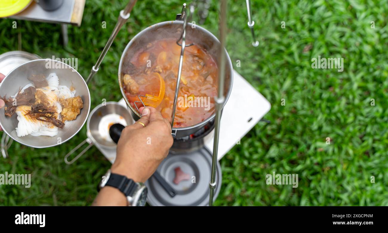 Campers lighting a fire while setting up the camp tent during their time in the nature. Cook food during lunch by hanging a pot to cook food. Stock Photo