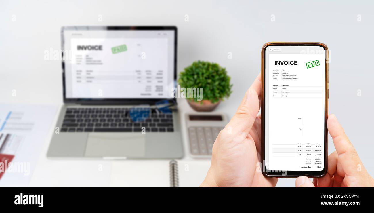 Digital Tax E Invoice Online Software On Laptop Screen. Close-up Of Businessperson Using Laptop While Paying Invoice On Mobilephone In Office. Stock Photo