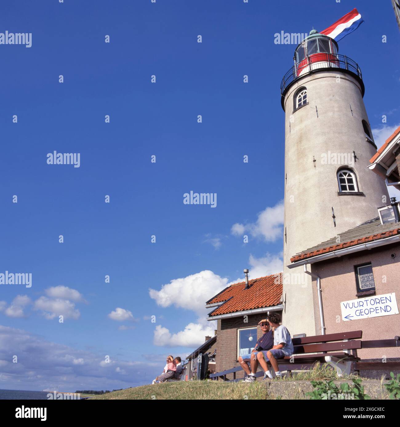 URK,HOLLAND-JULY 04, 2024:Urk Netherlands, lighthouse of Urk with the Dutch national flag on a bright summer day with people watching the lake ijsselm Stock Photo