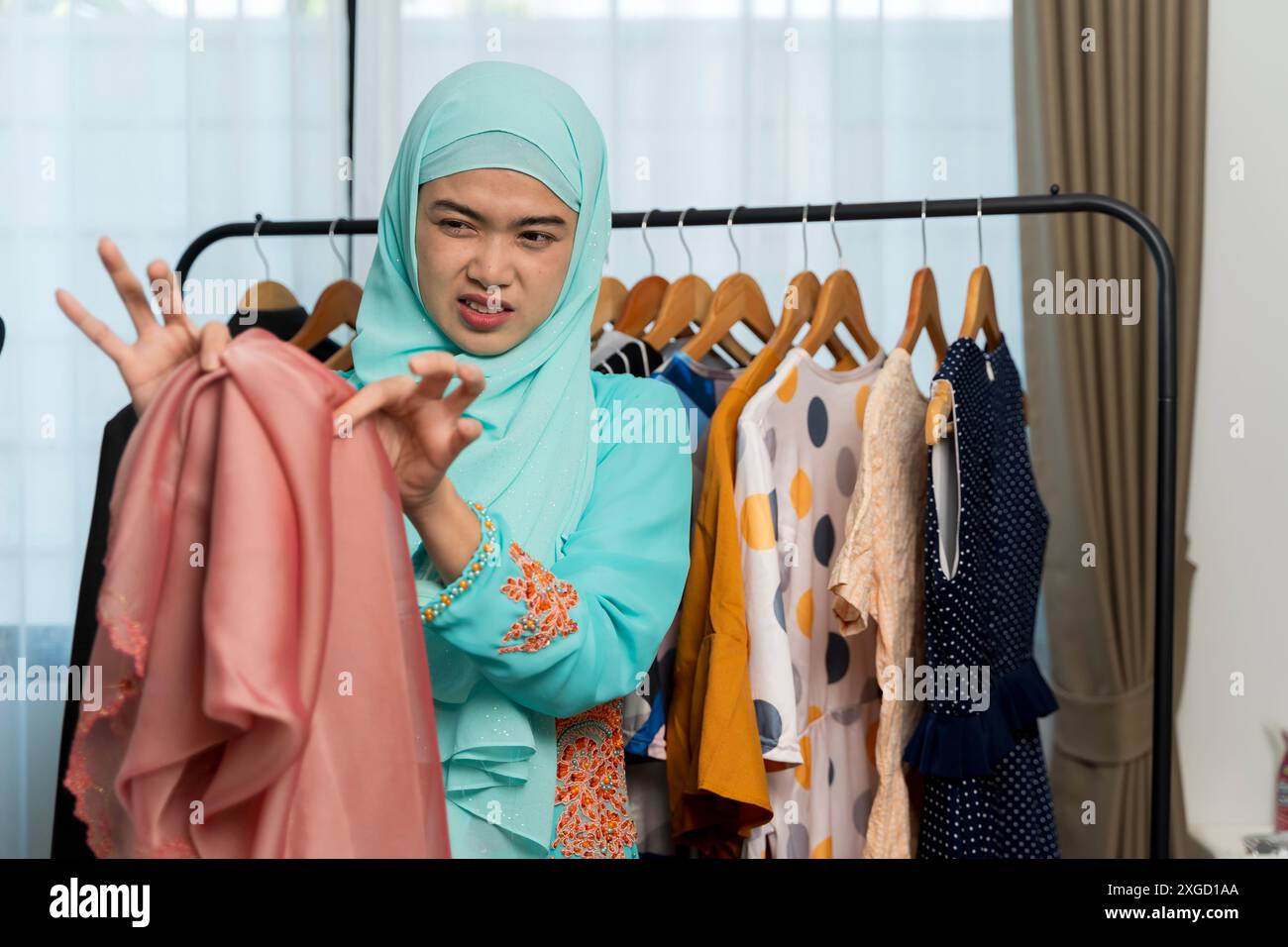 Young beautiful arab woman wearing islamic hijab is smelly stinky musty from clothes doing housework holding a smelly basket with clothes. Stock Photo