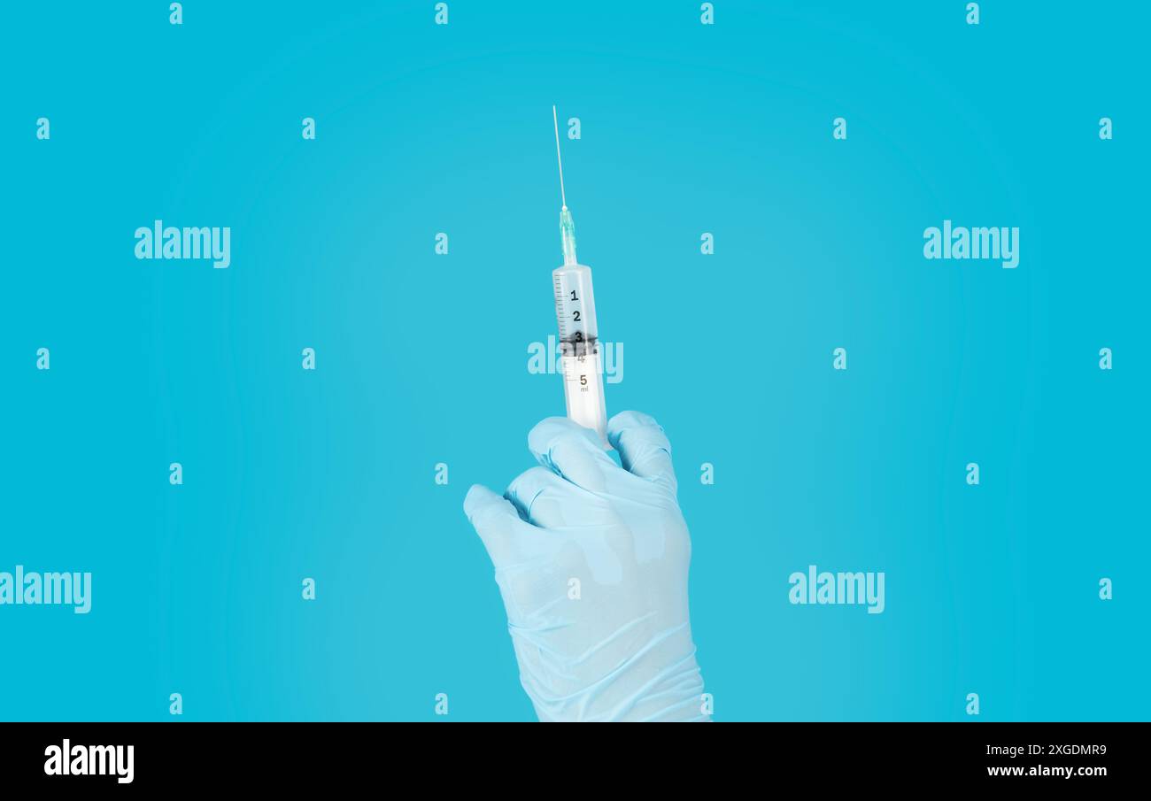 Gloved Hand Holding Syringe Against Blue Background Stock Photo - Alamy