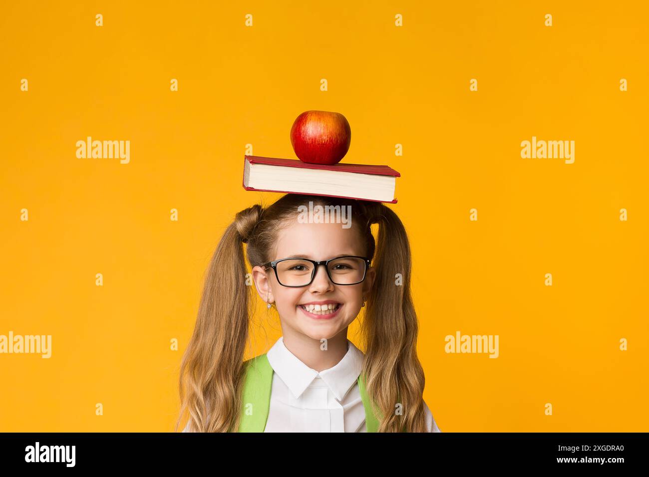 Schoolgirl Gesturing Thumbs-Up Holding Book And Apple On Head Stock ...