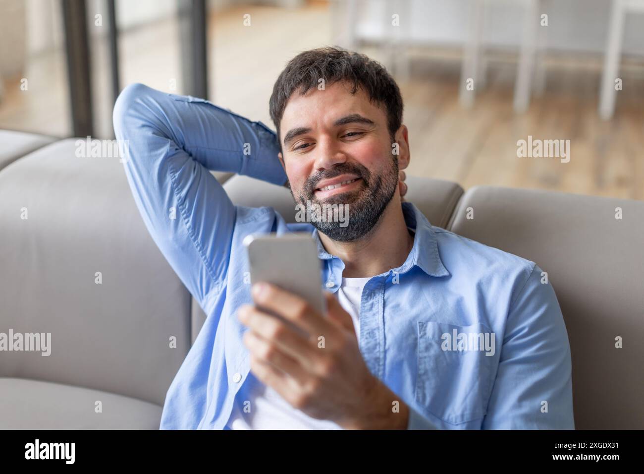 Smiling Man Using Smartphone While Relaxing on Couch Stock Photo