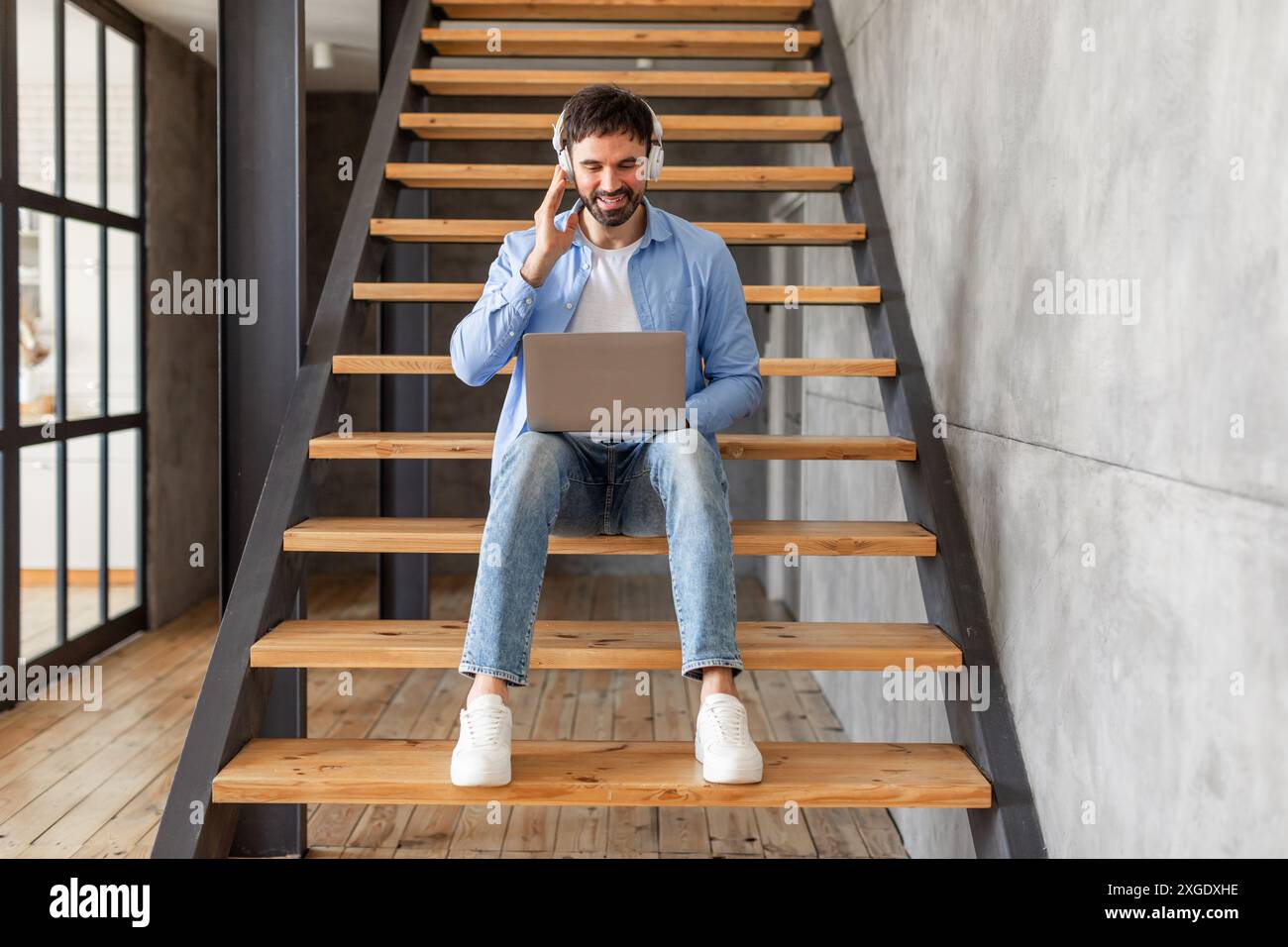 Man Using Laptop While Sitting On Indoor Stairs Stock Photo