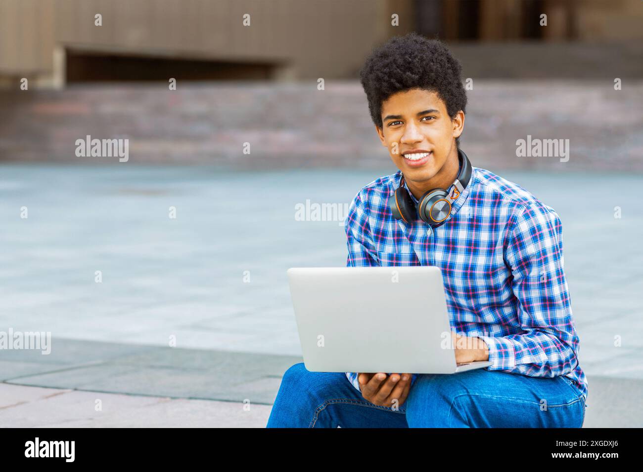 Teen Guy Smiling While Using Laptop Outdoors Stock Photo