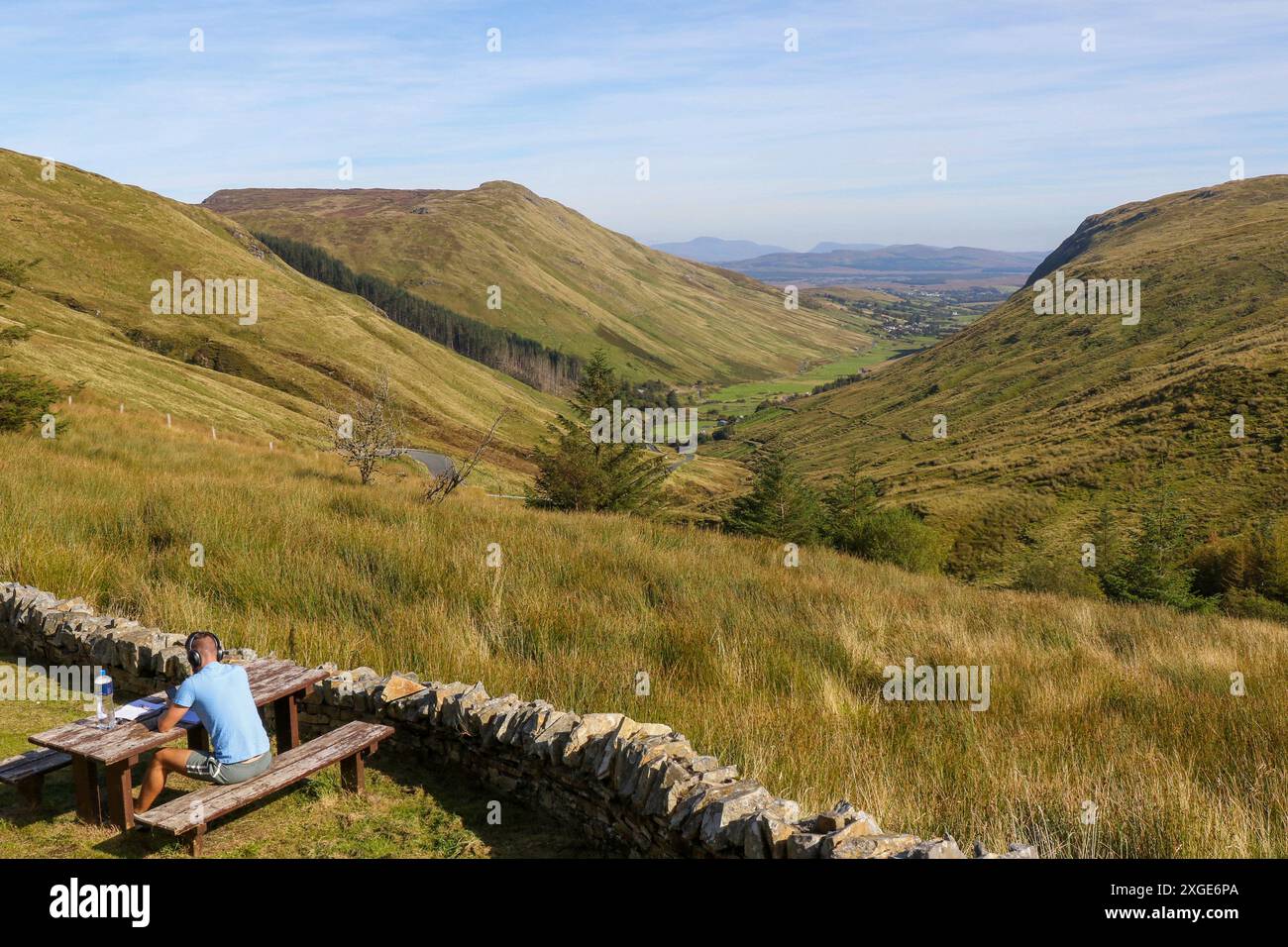 Young man wearing headphones picnic table Ireland overlooking scenic rural valley Glencolmcille County Donegal Ireland. Stock Photo