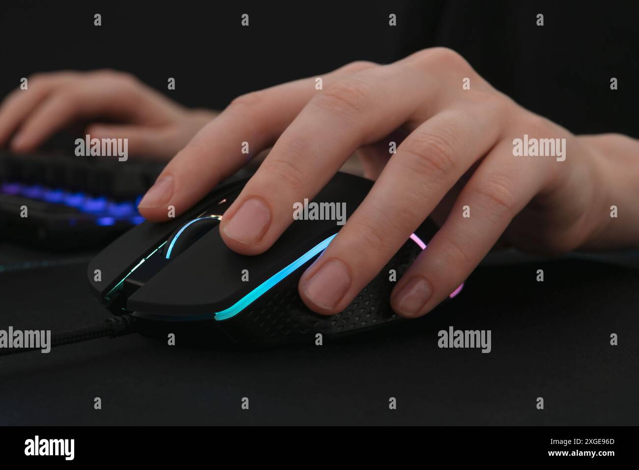 Gamer using modern wired computer mouse at dark table, closeup Stock Photo