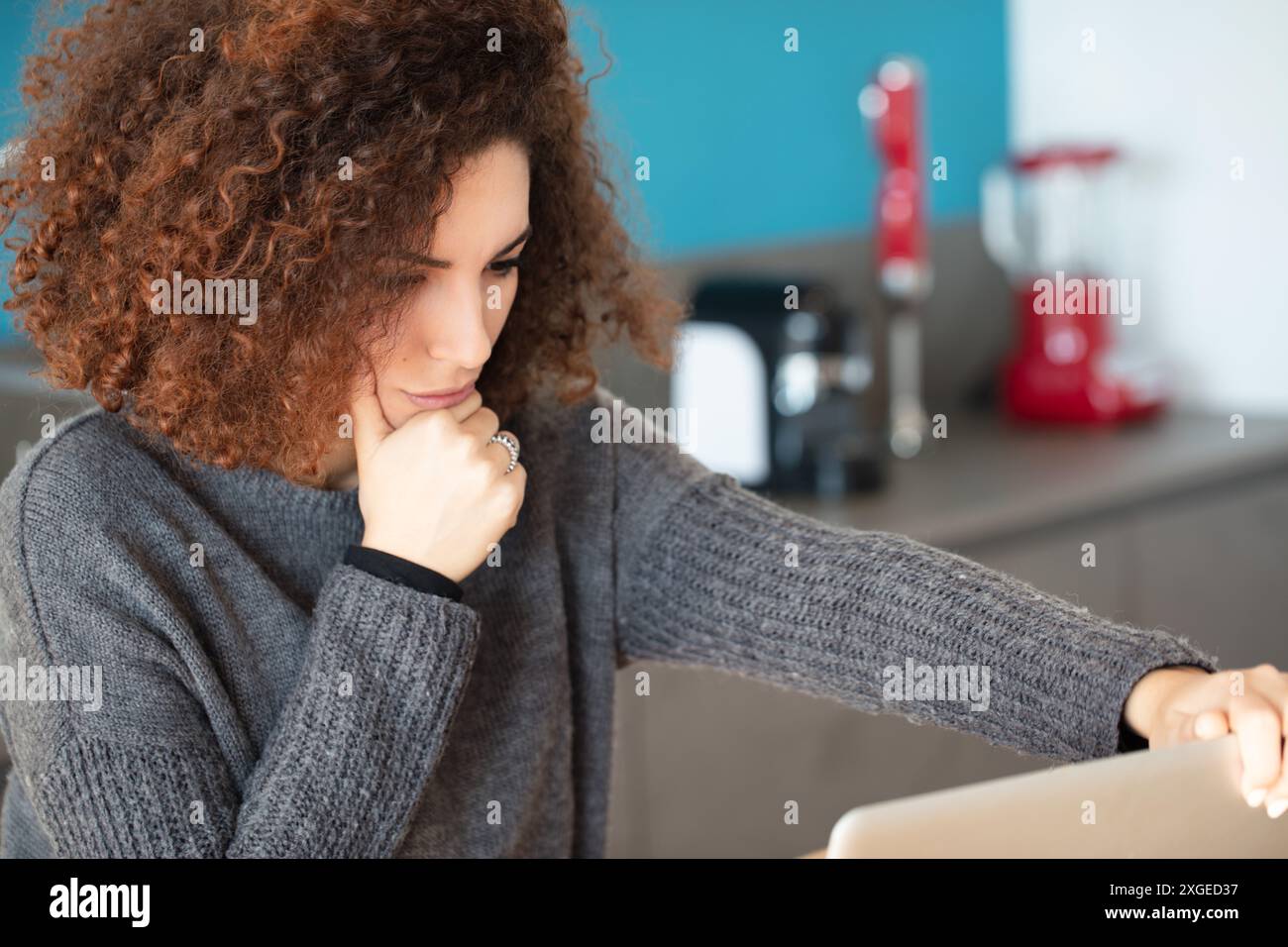 Concentrated and thoughtful a curly haired woman sits in her kitchen