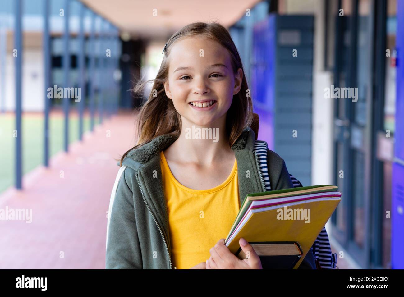Portrait of smiling caucasian schoolgirl holding books in school ...