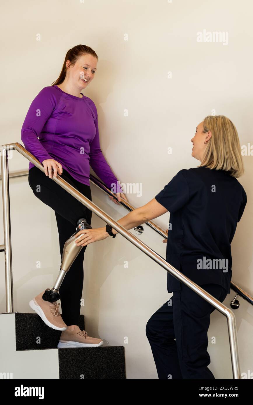 Woman with prosthetic leg walking up stairs with therapist assisting Stock Photo