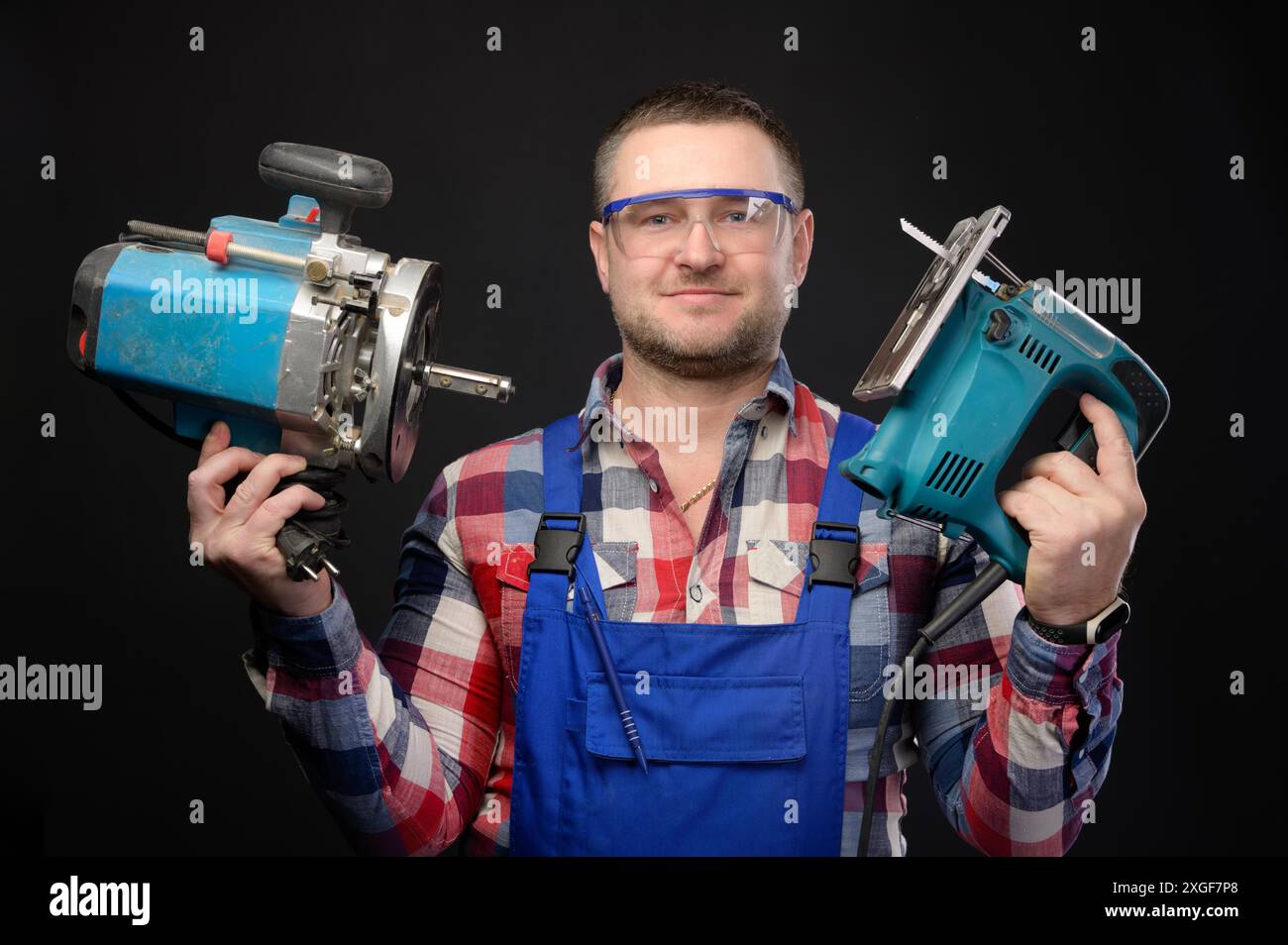 Caucasian repairman in goggles holding woodworking tools. Carpenter portrait on black studio background Stock Photo