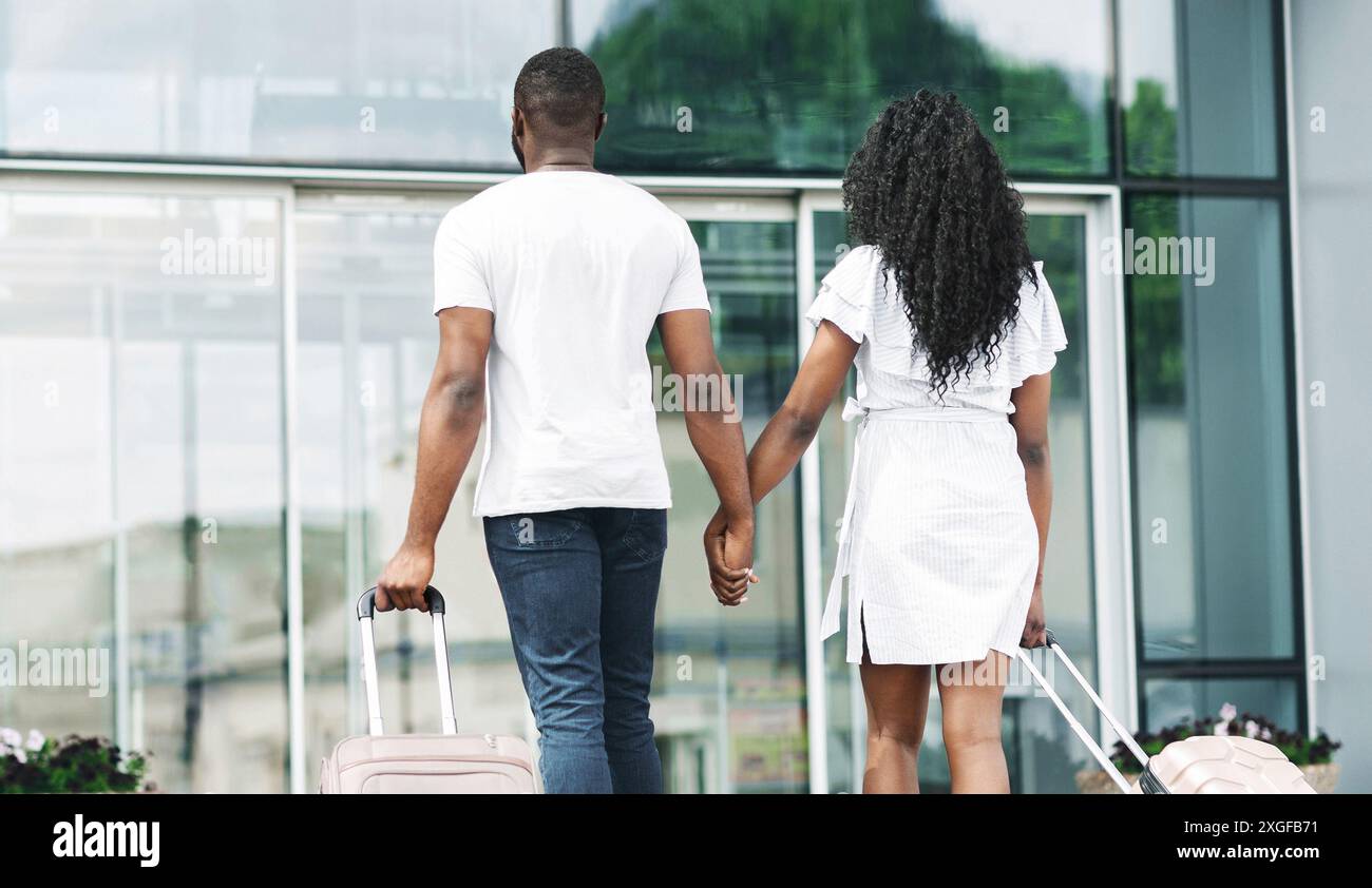 Couple Walking Away From Airport Entrance With Luggage, Back View Stock ...
