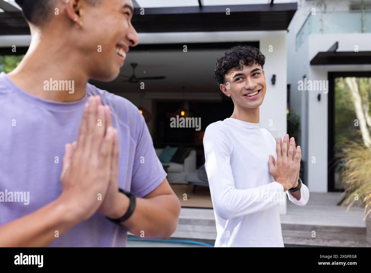 Smiling men greeting each other with namaste gesture outside modern home Stock Photo