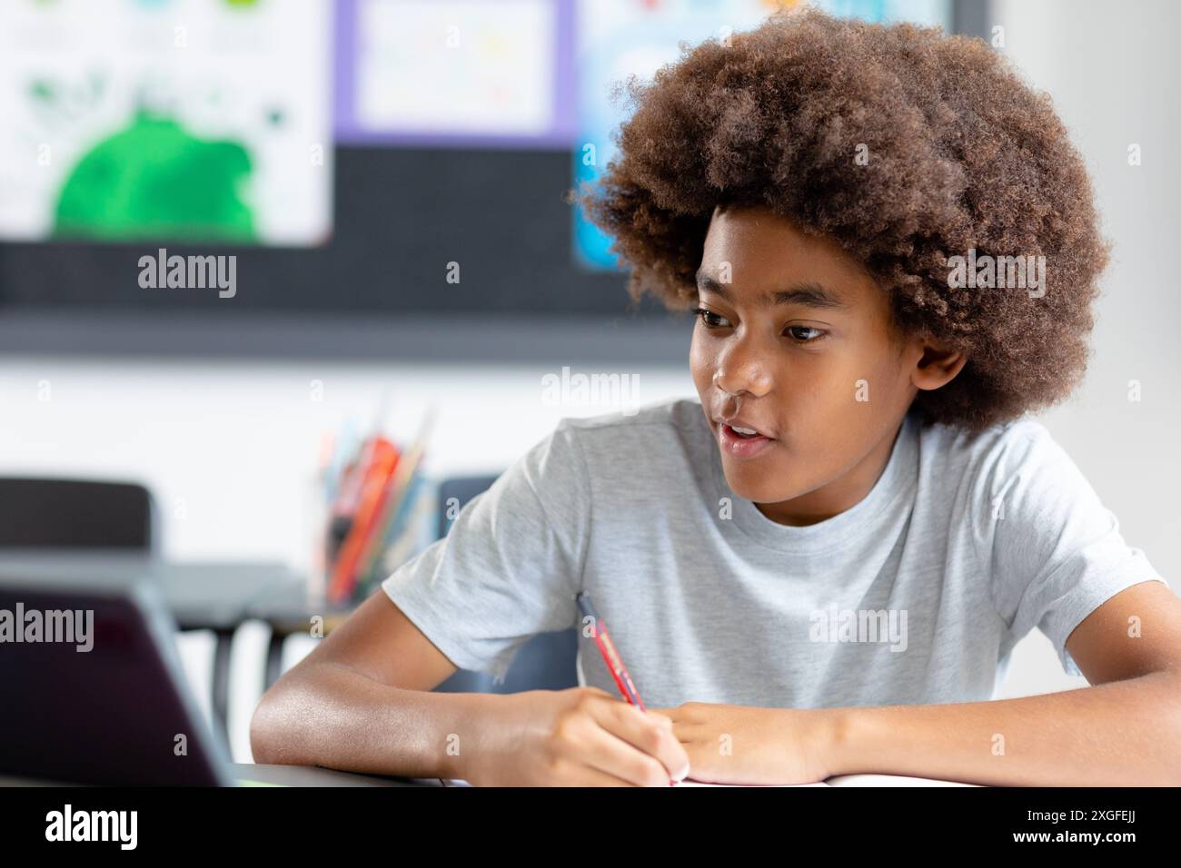 Happy african american schoolboy with afro sitting at desk in class ...