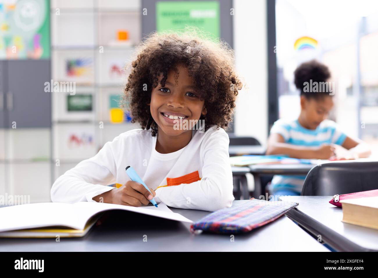 Portrait of happy african american schoolboy sitting at desk in school ...