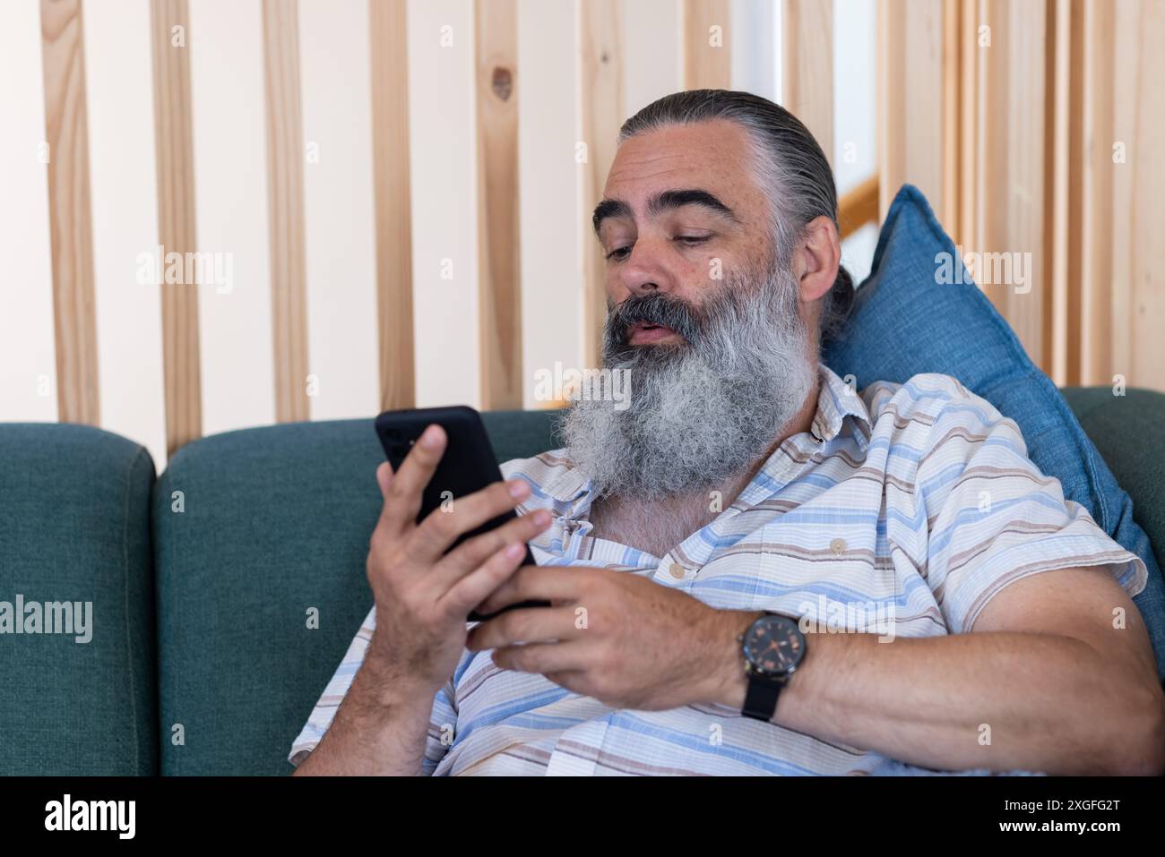 Using smartphone, bearded senior man relaxing on couch, checking messages Stock Photo