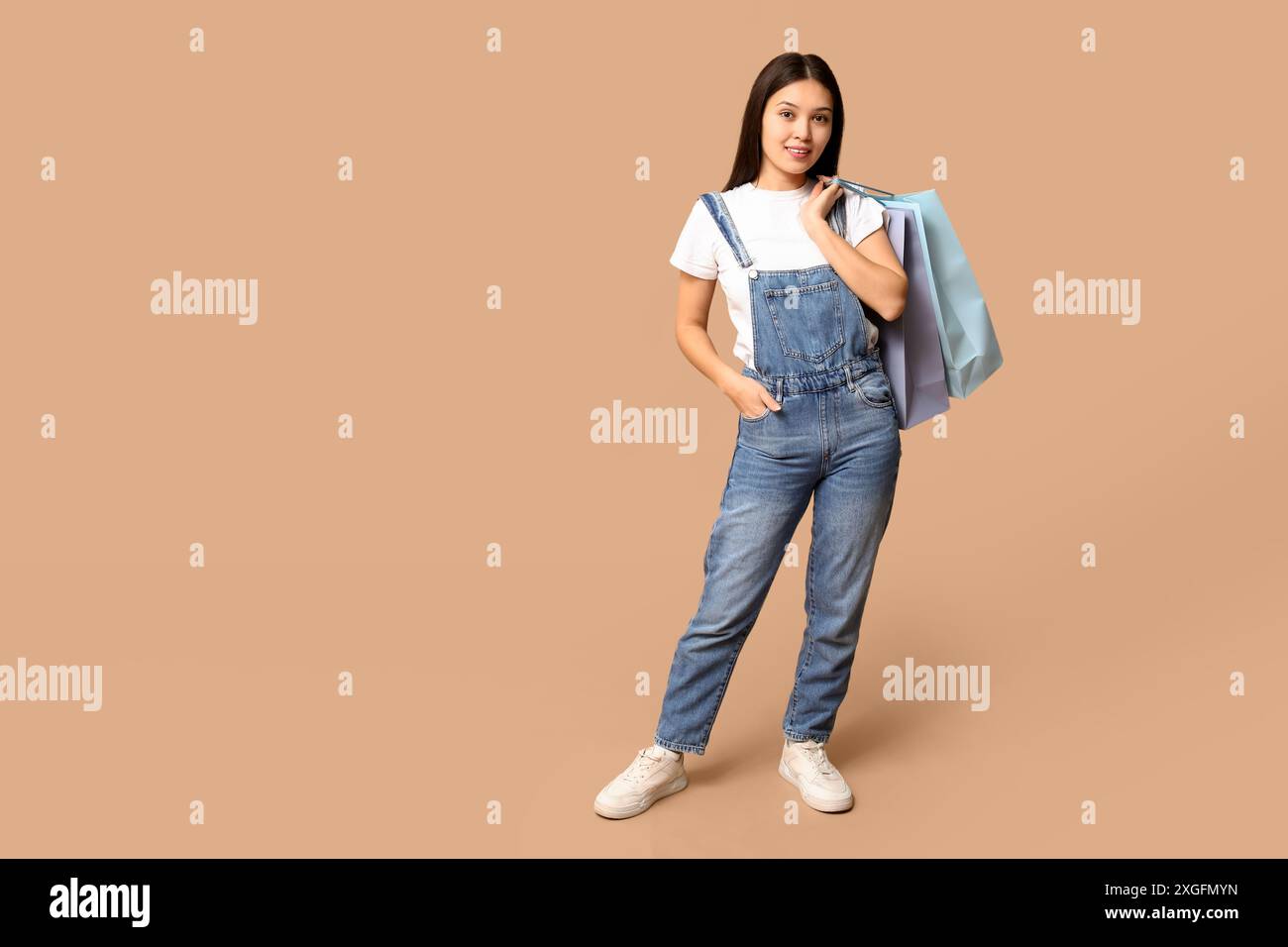 Fashionable young Asian woman in stylish denim overalls with shopping ...