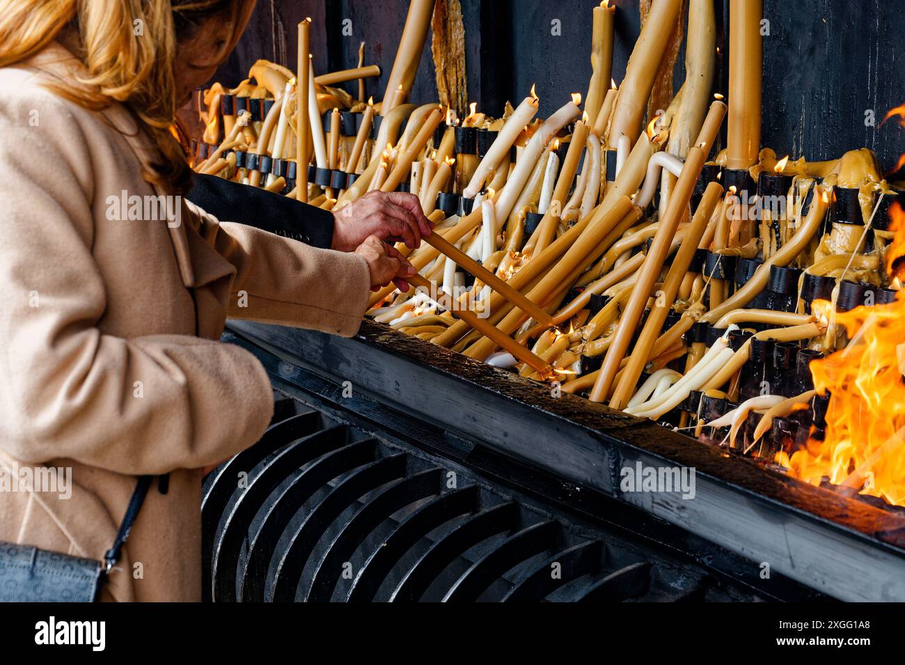 At the fatima sanctuary, visitors light tall candles, their hands carefully placing the wicks into the flames Stock Photo