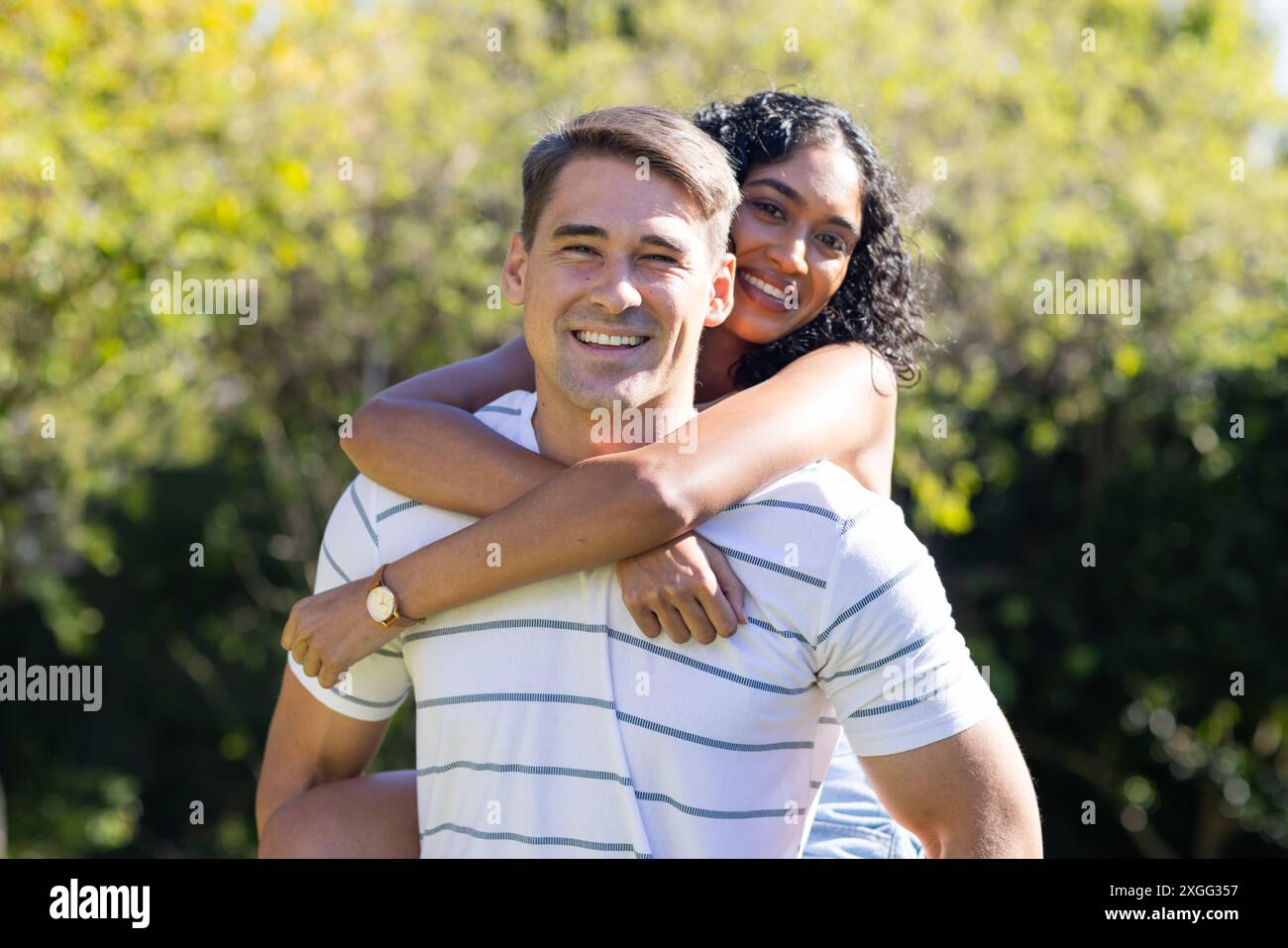 Smiling young couple enjoying piggyback ride outdoors in sunny park ...