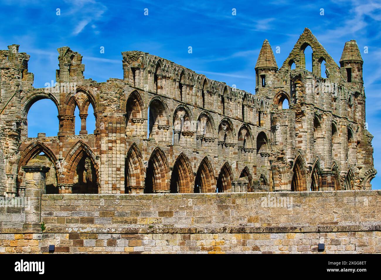 A historic stone abbey ruin with arched windows and intricate architectural details against a blue sky, Whitby Abbey, Whitby, Yorkshire, England, Unit Stock Photo