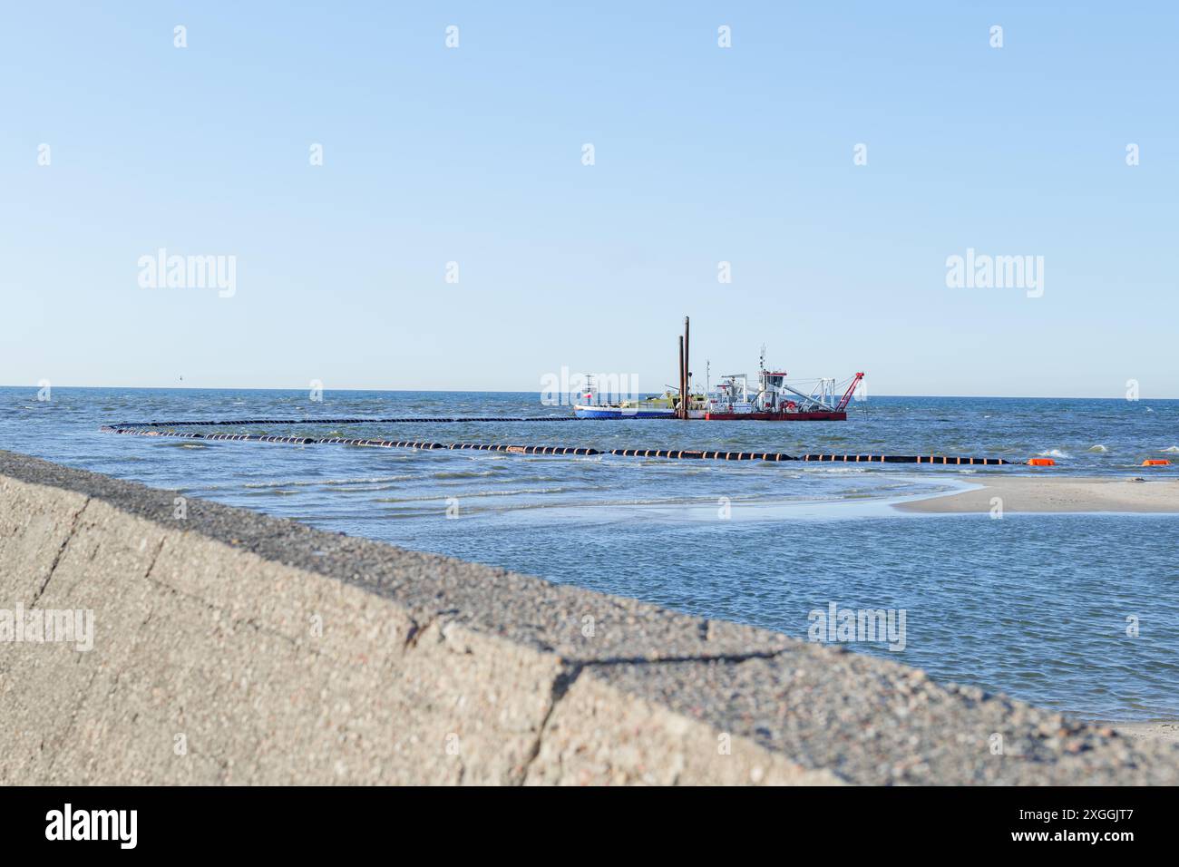 Marine works on dredging the bottom of the Baltic Sea. Two dredger ships with crew at work on sunny, summer day. The concrete lining of the pier in th Stock Photo