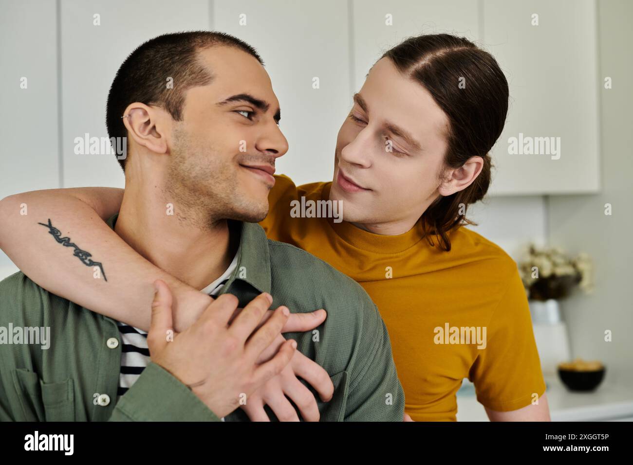 Stand Close A young gay couple stands close together in a modern apartment, their ...