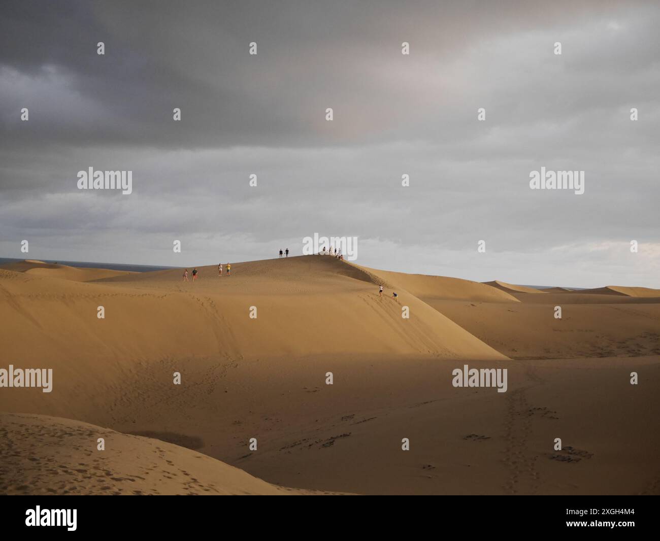 A group of people explore sand dunes under a dramatic sky. Their ...