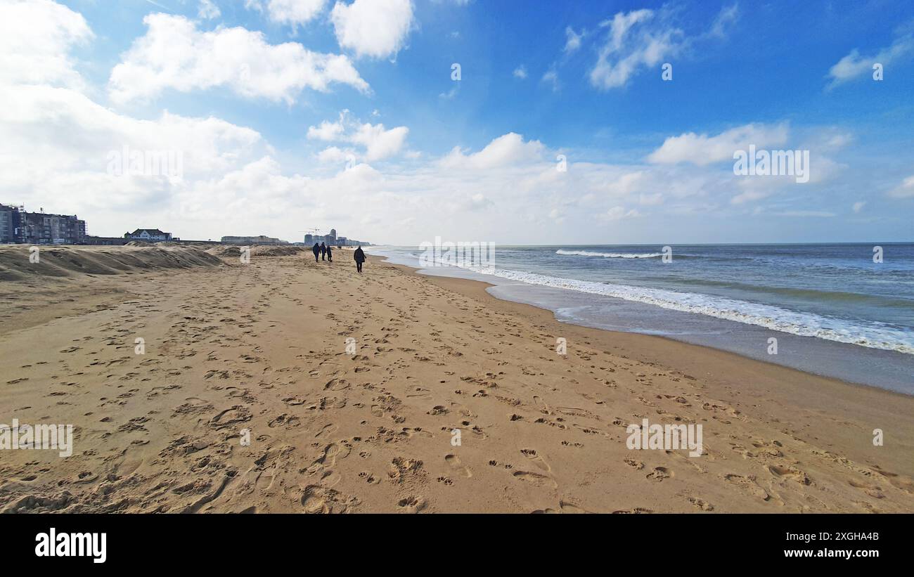 People walking near the sea. Walking way on the beach. Much sand, water and sky near the hotel. Stock Photo