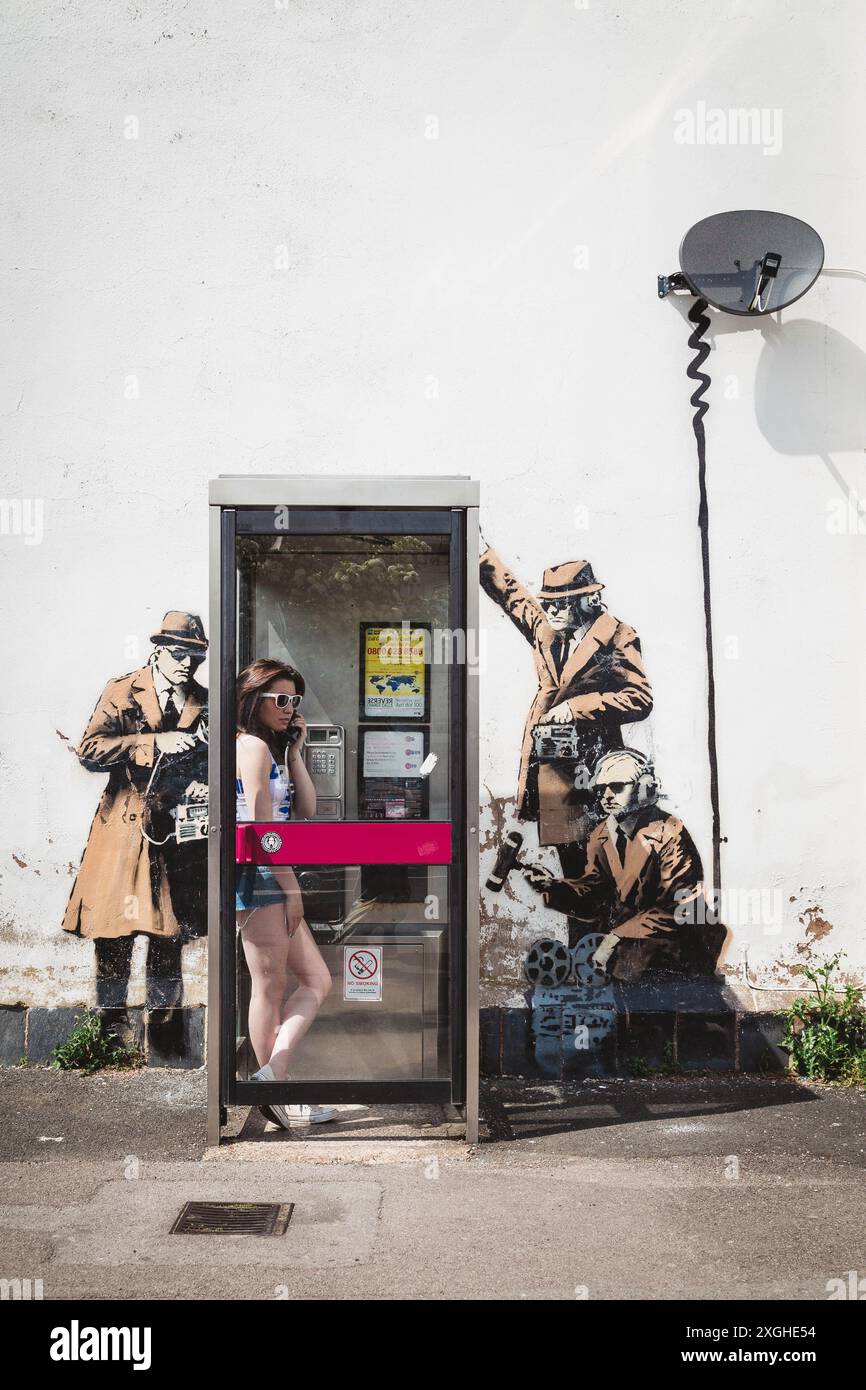 Young Woman in a Phone box Surrounded by the Banksy Wall Art Spy Booth in  Cheltenham Stock Photo - Alamy