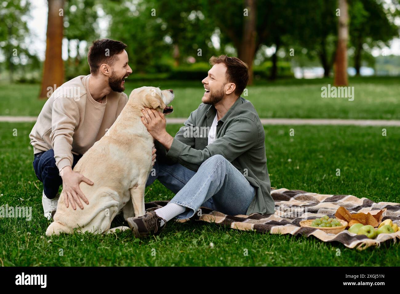 A bearded gay couple enjoys a picnic with their labrador dog in a park. The men are laughing and petting their dog, creating a heartwarming scene. Stock Photo