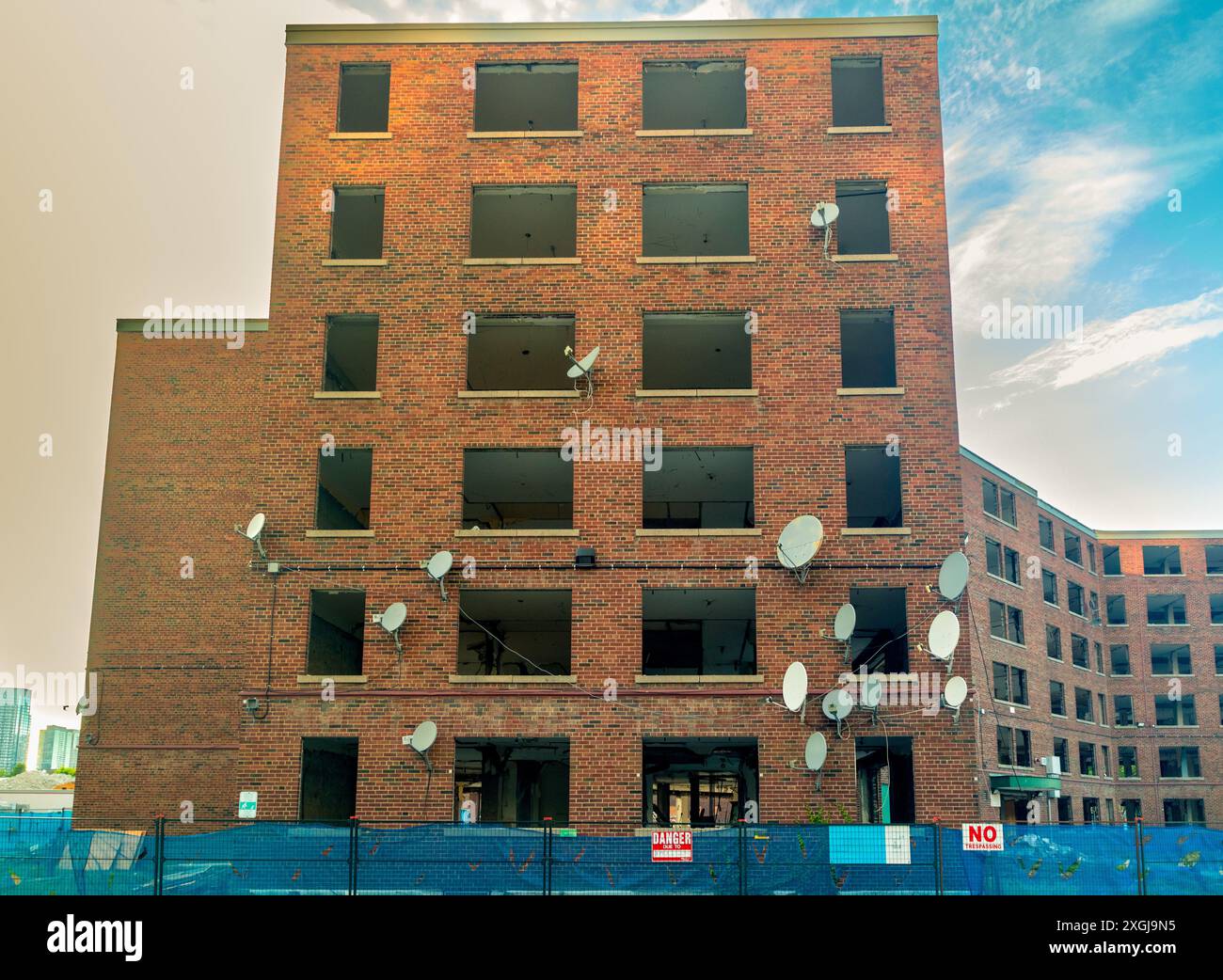 Now useless satellite dishes dot an abandoned apartment building with windows removed. Exposed brickwork and interiors and glimpse of modern replaceme Stock Photo