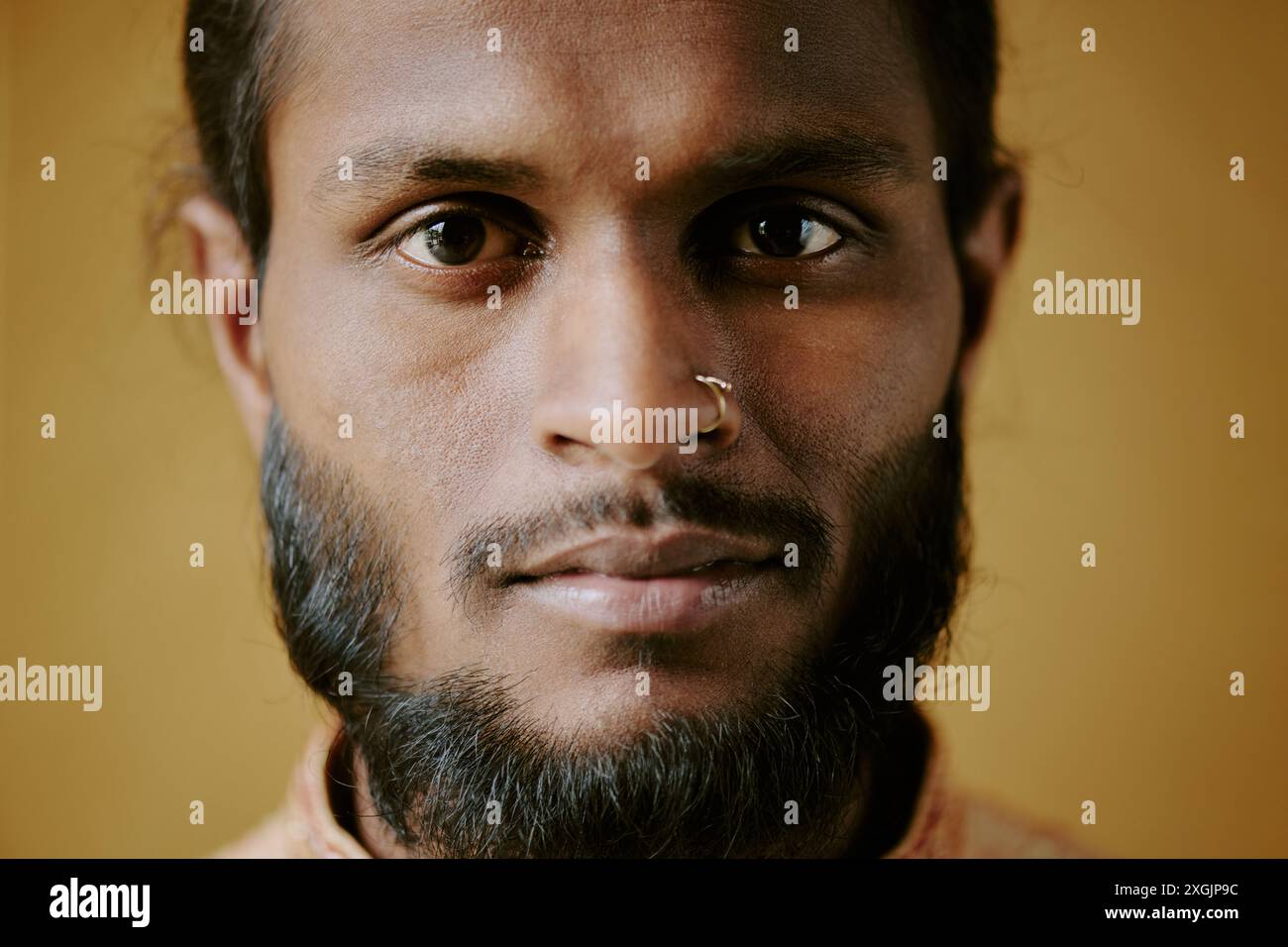 Close up of young Indian man smiling gently while staring at camera Stock Photo