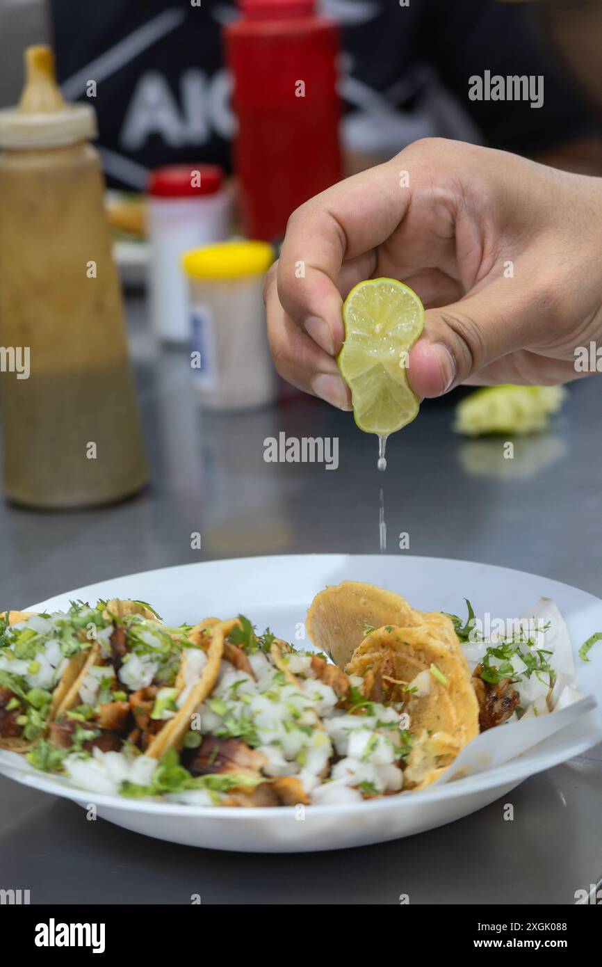 Close-up of a hand squeezing fresh lime over a plate of delicious street tacos topped with cilantro and onions. Perfect for depicting authentic Mexica Stock Photo