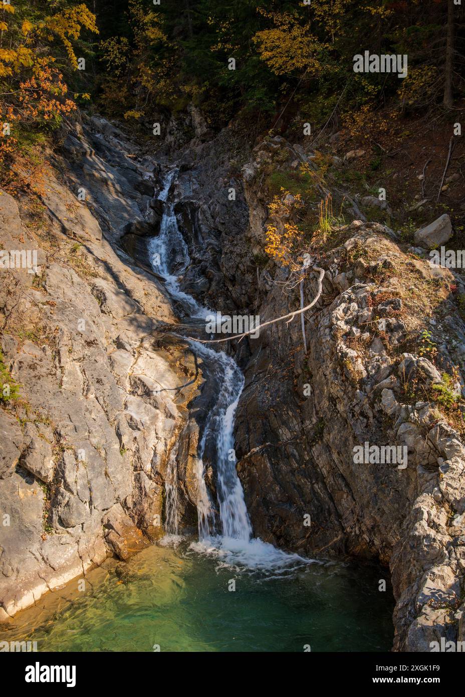 Small waterfall cascading down a rocky mountainside in autumn, creating a pool of green water at the bottom Stock Photo