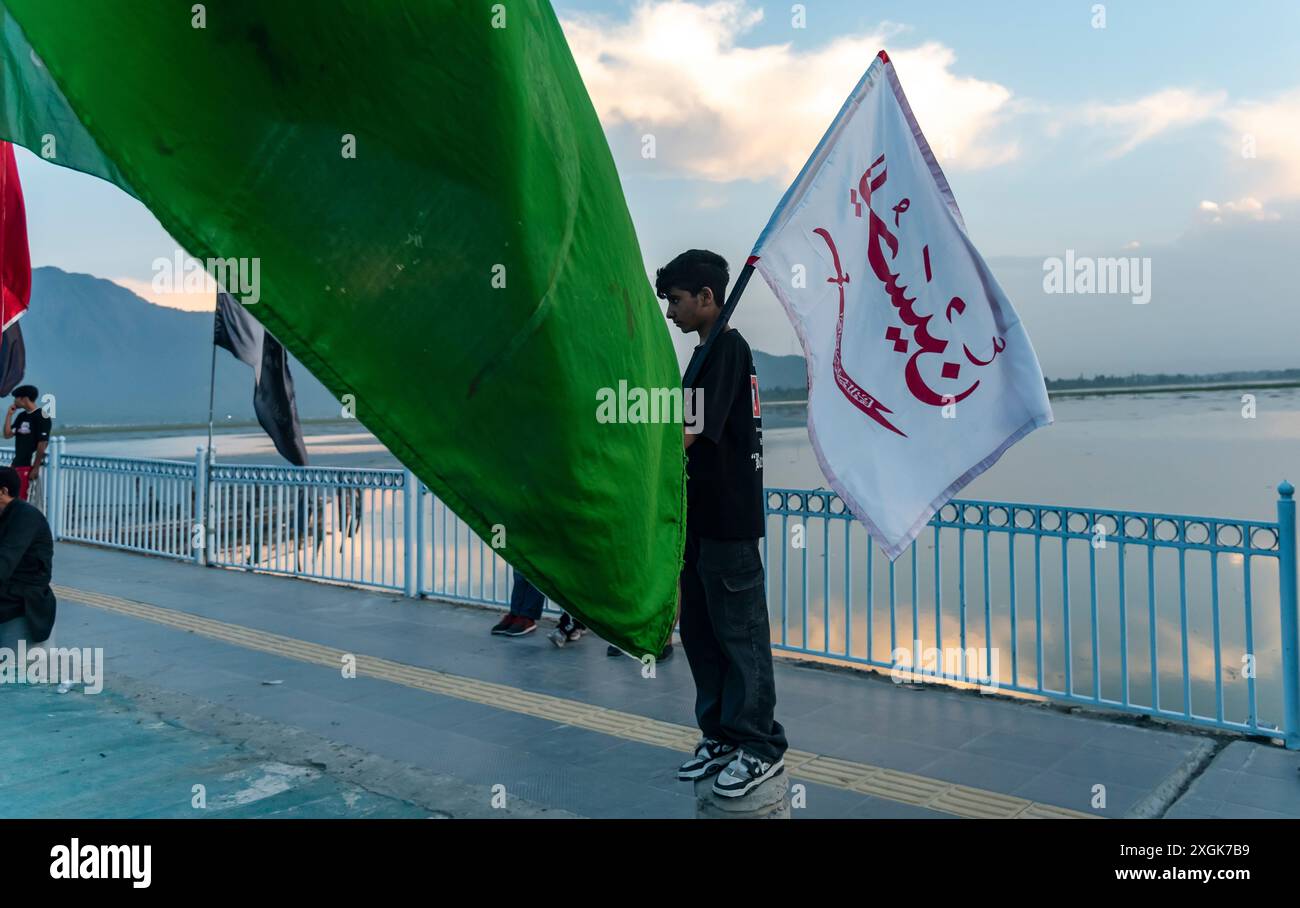 A Kashmiri Shia Muslim boy holds a religious flag as he watches a tall ...