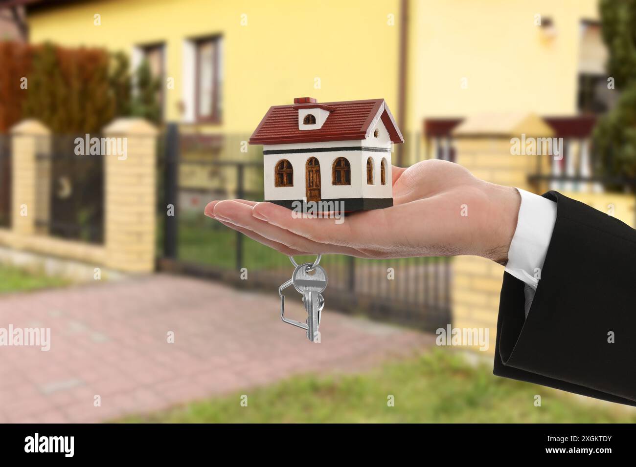 Real estate agent holding house model and key against future dwelling ...