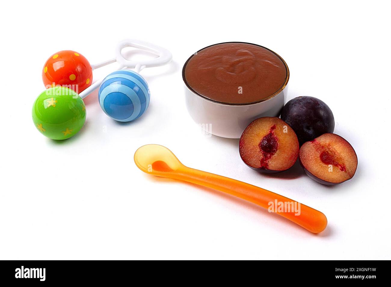 Baby food, plum puree, on a white background, with a spoon and a rattle ...