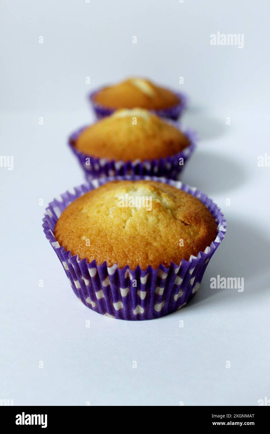 Three cupcakes in purple liners arranged in a row on a white surface Stock Photo