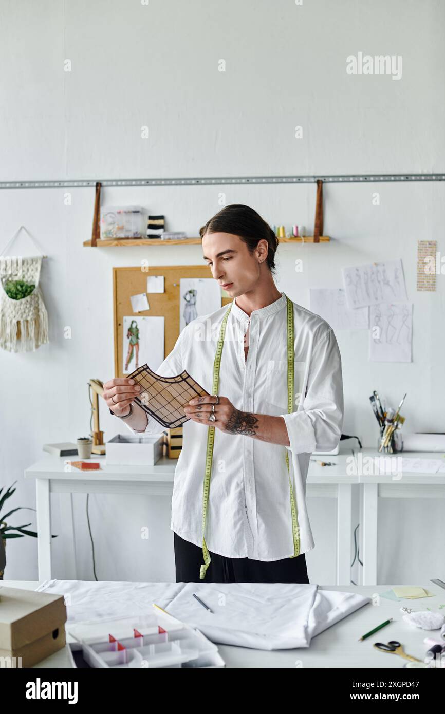 A young tailor in a white shirt examines a fabric pattern at his ...