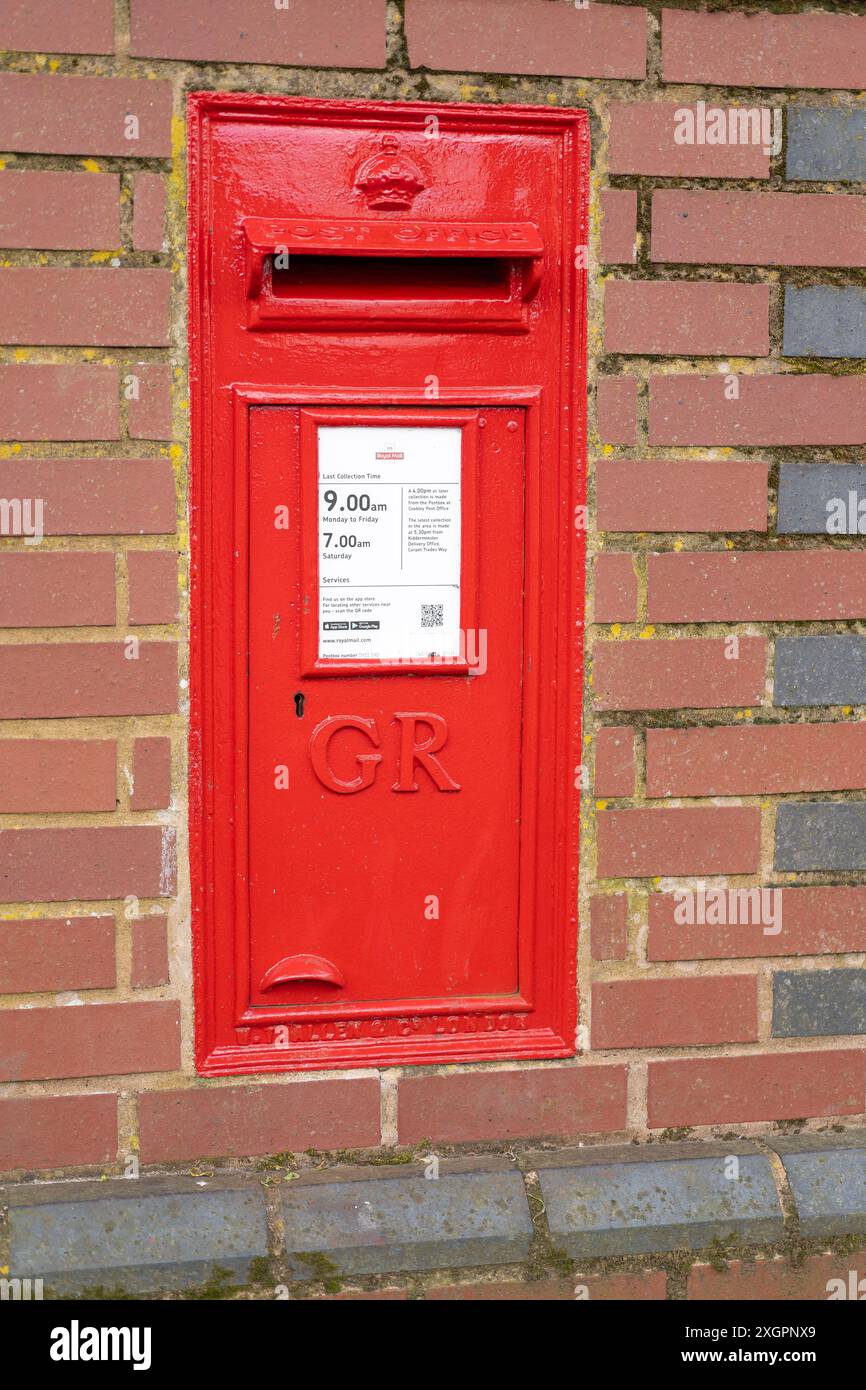 Close up of a red, Royal Mail post box/ letter box with the royal cypher letters GR on the front, set in a traditional brick wall outdoors, UK. Stock Photo
