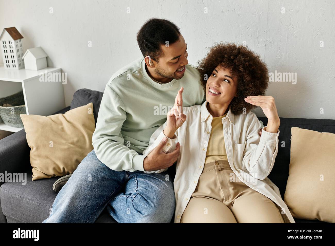 A loving African American couple sits on a couch, using sign language to communicate. Stock Photo
