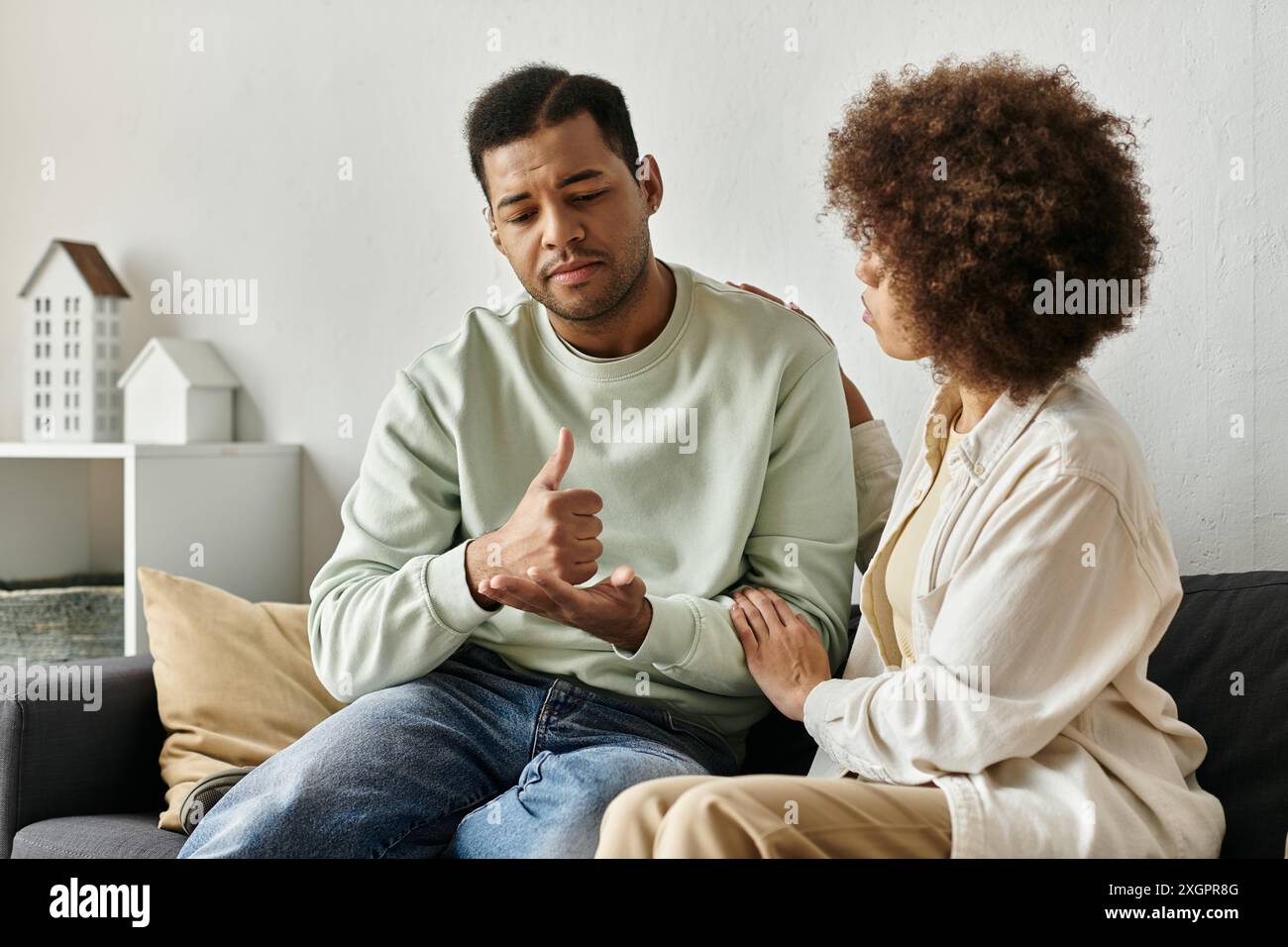 An African American couple communicates using sign language while sitting on a couch at home. Stock Photo