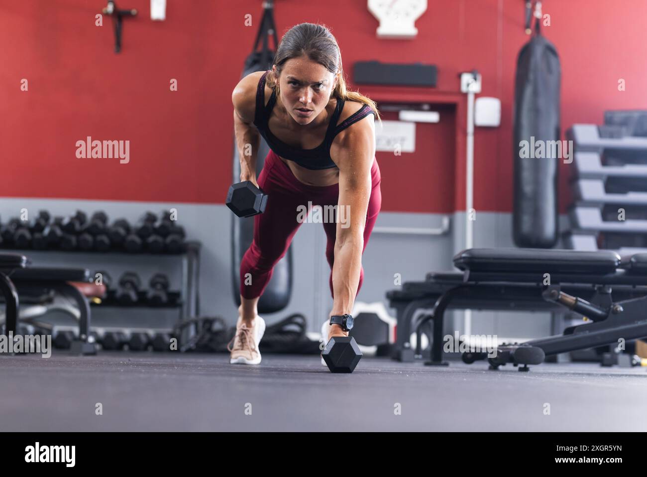 Fit young Caucasian woman performs a dumbbell workout at the gym. Her intense focus exemplifies dedication to fitness. Stock Photo