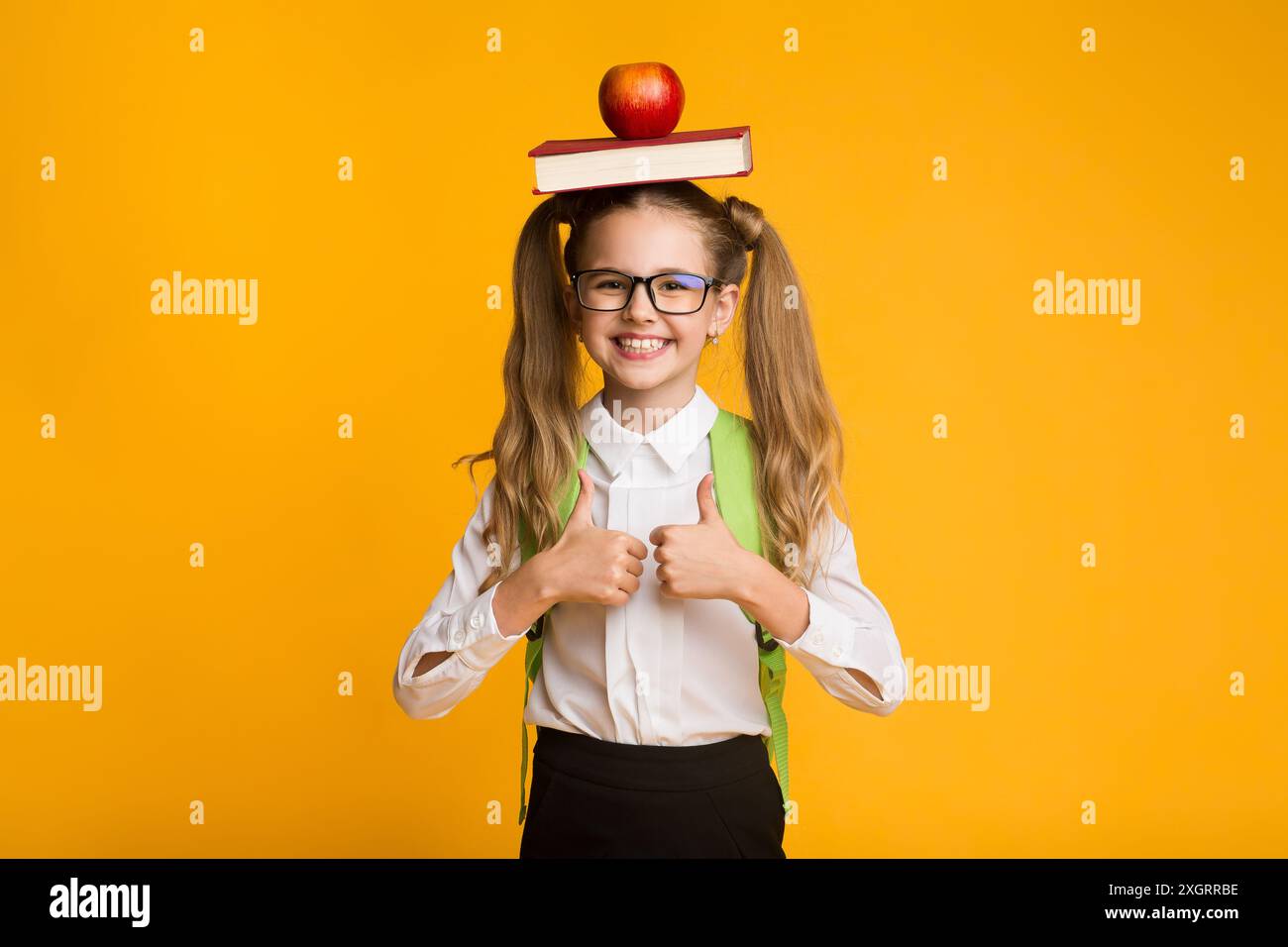 Schoolgirl Gesturing Thumbs-Up Holding Book And Apple On Head Stock ...