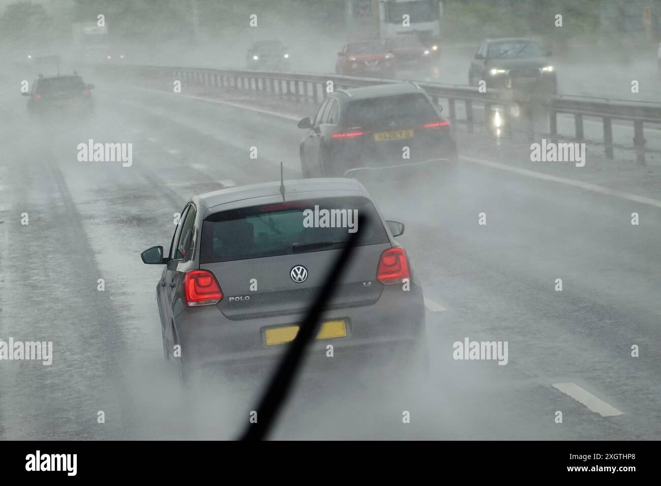 Widely reported in UK press was the unseasonal wet summer weather in mid June & early July 2024. Coach tour passengers on a summer holiday excursion witnessed these torrential rainfall driving conditions on M4 motorway viewed through front windscreen from the upper level. The driver out of sight at the lower level relying on window wipers, the top section seen here providing good vision of the VW car amongst raining weather & motorway spray gloom. Stock Photo