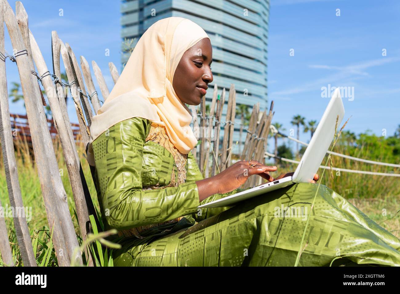 A young Muslim woman in a hijab is focused on working with a laptop ...