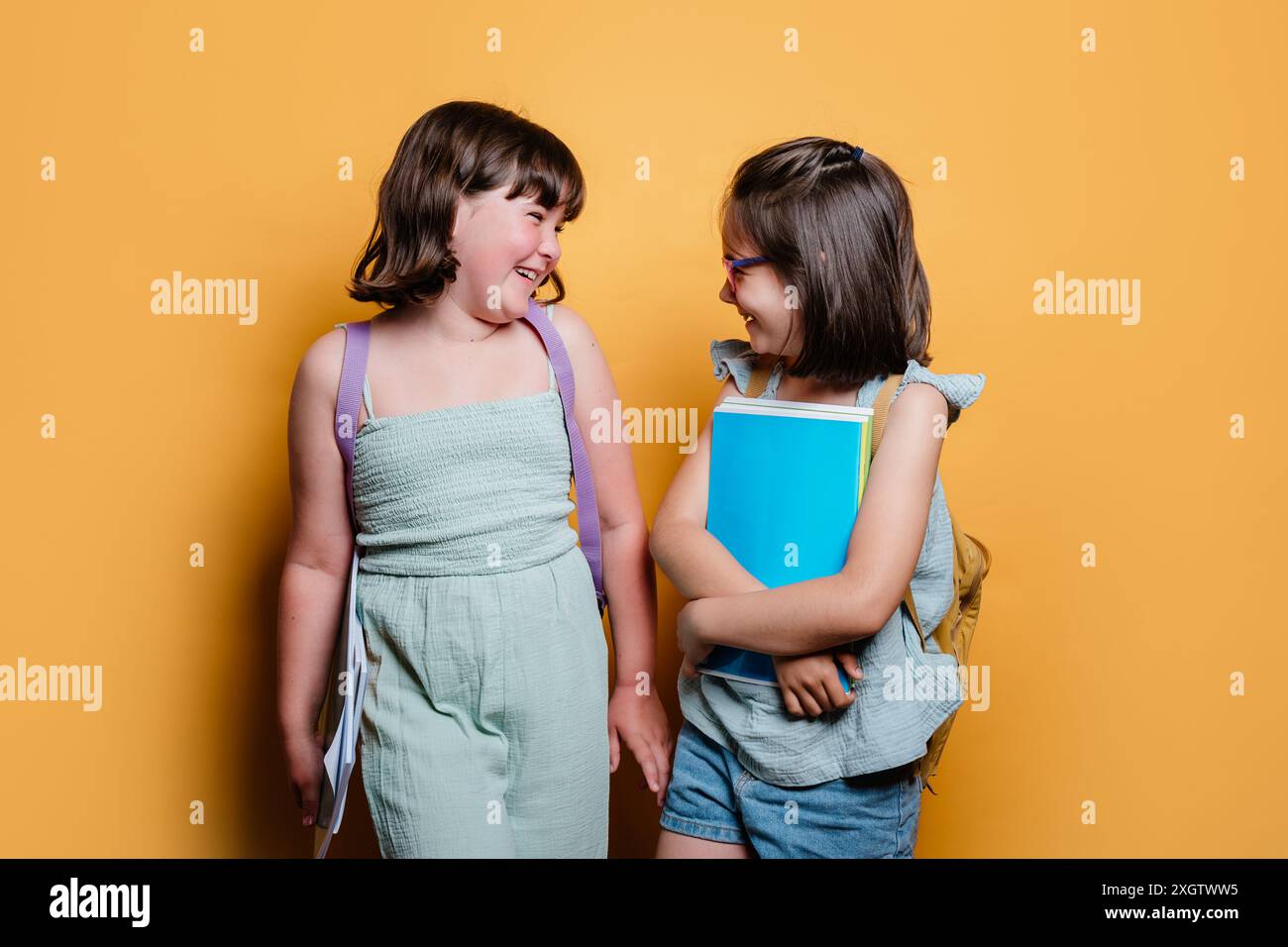 Two happy schoolgirls, one looking at the other with a smile, holding ...