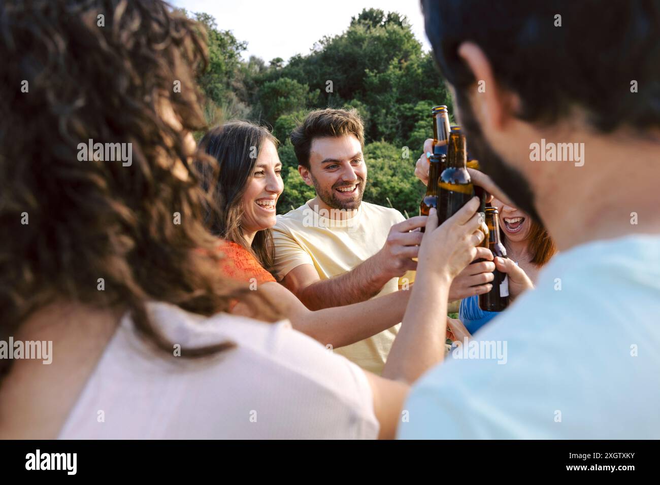 A cheerful group of friends toasting with beers in an outdoor setting ...